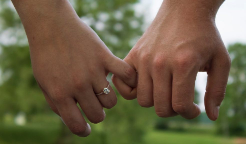 A couple holding hands with female wearing an engagement ring