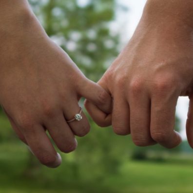 A couple holding hands with female wearing an engagement ring